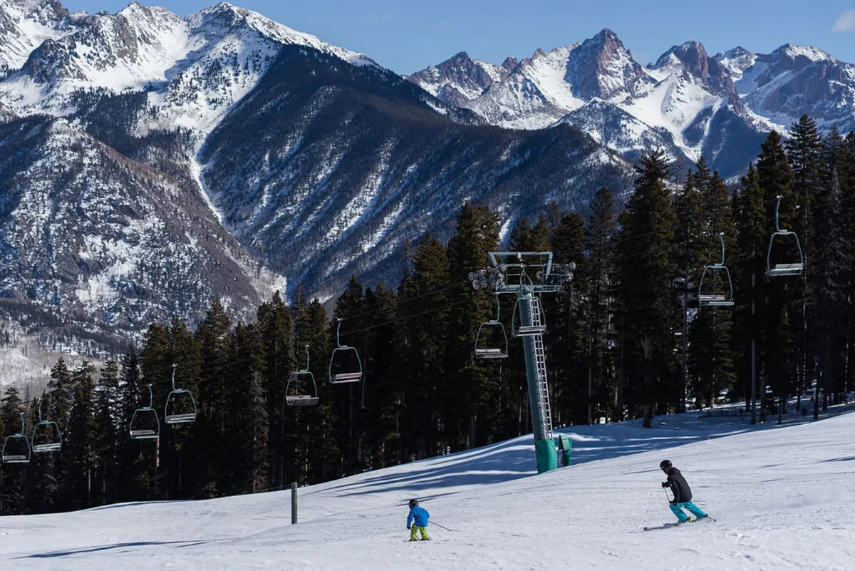 A lively scene featuring skiers gliding down a snow-covered mountain slope, with the ski lift visible in the background and panoramic views of the surrounding peaks. The image captures winter adventure just steps away from the property.