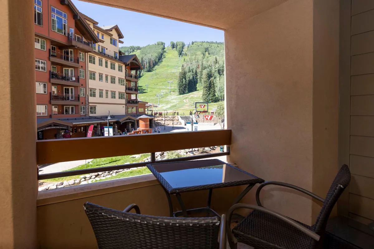 A serene balcony view overlooking the mountain slope and outdoor seating area, with easy sightlines to the ski lifts and a vibrant village atmosphere. The space invites guests to relax while soaking in the alpine environment.