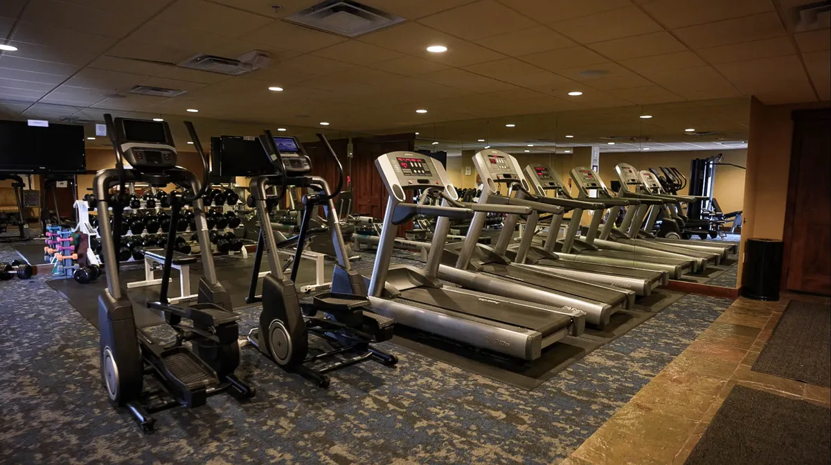A well-equipped fitness center with treadmills, elliptical machines, and a dumbbell rack, set in a bright, modern room designed for both solo and group workouts. The energetic, uplifting atmosphere encourages activity and health.